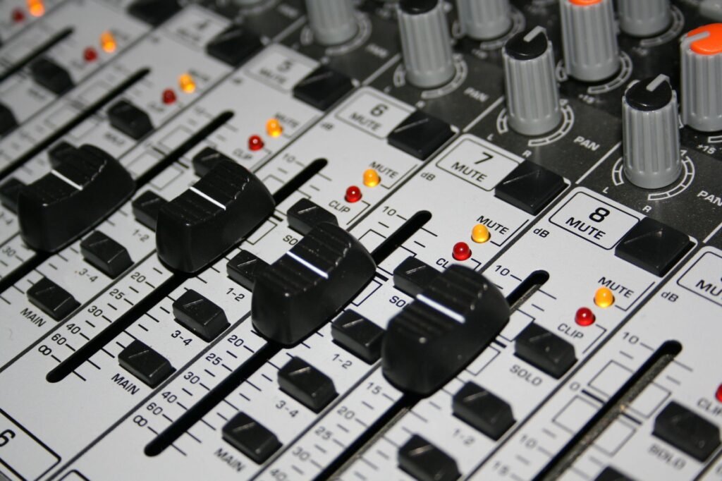 Detailed shot of a professional audio mixer with knobs and sliders illuminated by indicator lights.