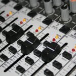 Detailed shot of a professional audio mixer with knobs and sliders illuminated by indicator lights.