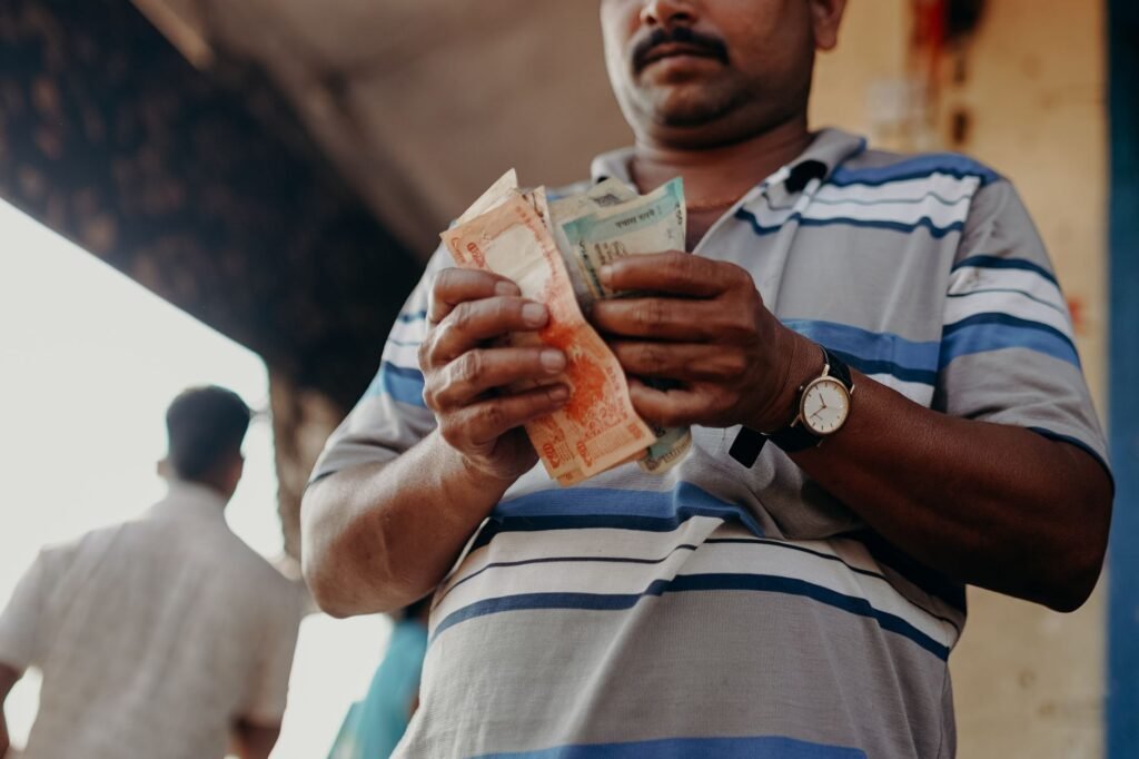 Man in Indian market counting rupee notes, showcasing daily street commerce.