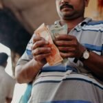 Man in Indian market counting rupee notes, showcasing daily street commerce.