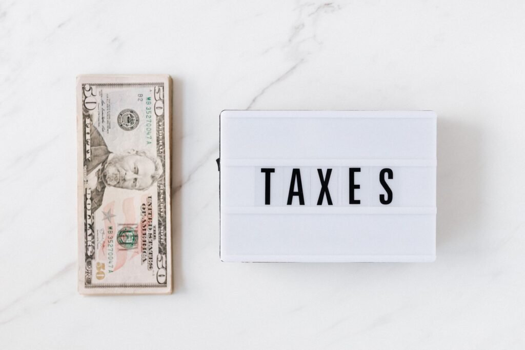 Top view composition of stack of American dollars placed on white marble surface with white retro light box with TAXES inscription