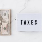 Top view composition of stack of American dollars placed on white marble surface with white retro light box with TAXES inscription