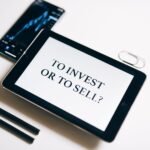 A tablet with text 'To Invest or To Sell?' on a white background.