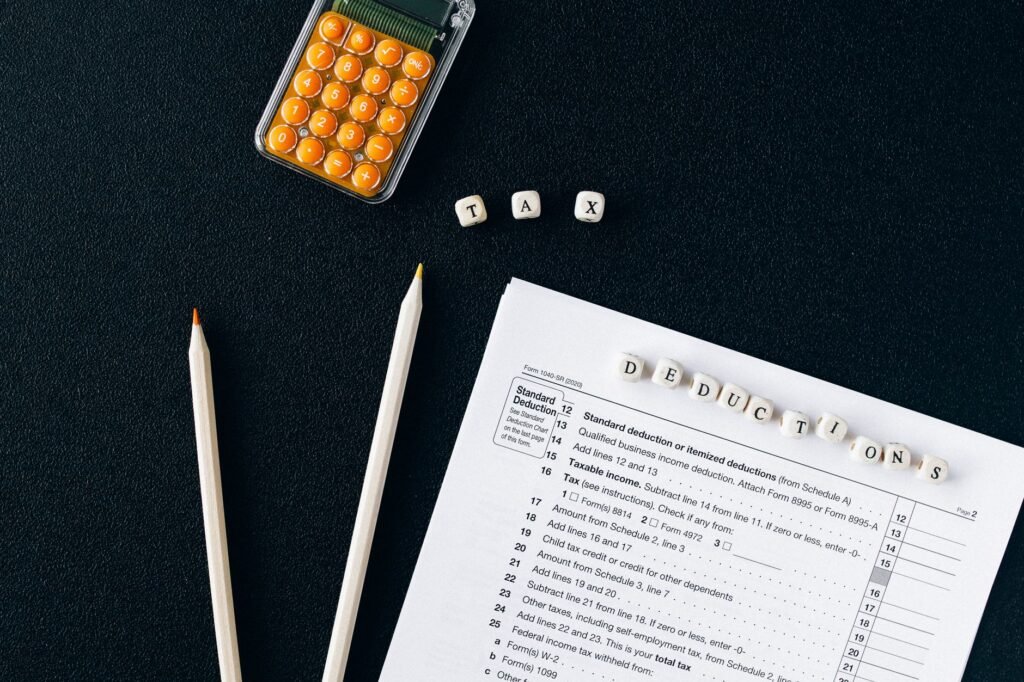 Flat lay of tax form, pencils, and calculator on black background, emphasizing tax deductions.