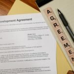 Close-up of a development agreement document with pen and Scrabble tiles spelling 'AGREEMENT.'