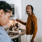 Young black couple in casual outfit standing at kitchen and arguing with each other at home