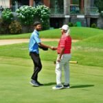 Two golfers shake hands on a lush green course in Hyderabad, India, celebrating their game.