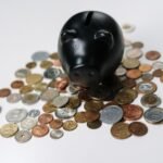 Black piggy bank surrounded by a variety of coins on a white surface, symbolizing savings and finance.