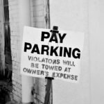 A black and white photo of a pay parking sign in downtown Tyler, Texas. Violators will be towed.