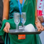 A server in formal attire presenting glassware on a tray during a professional event.