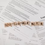 Top view of scrabble tiles spelling 'DOCUMENTS' on various contracts and agreements.