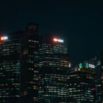 Illuminated city skyscrapers of major banks in Singapore's financial district at night.