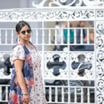 Modern woman in sunglasses poses by a decorative white metal gate on a sunny day.