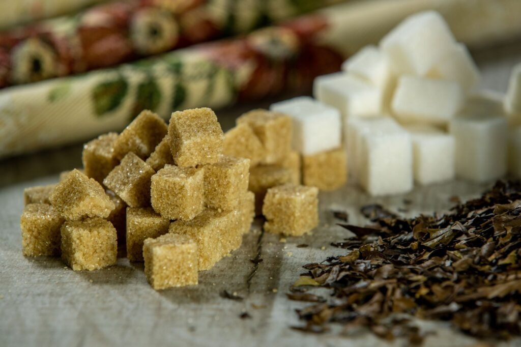 Close-up of brown sugar cubes, white sugar cubes, and tea leaves on a wooden surface.