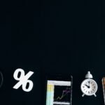 Flat lay of financial analysis tools including phone, clock, and calculator on black background.