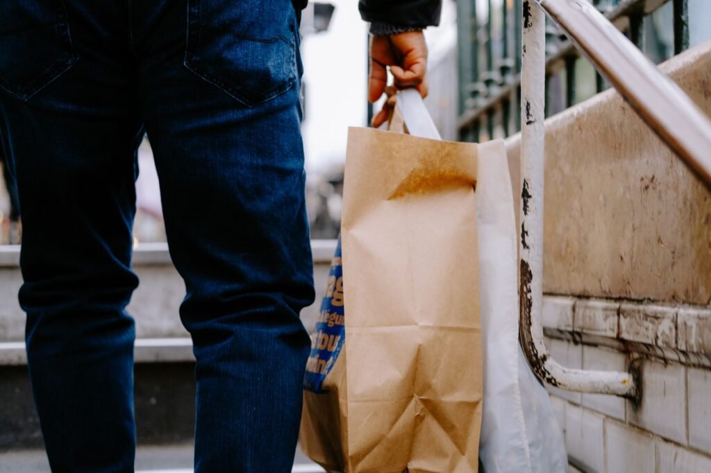 Close-up of a person carrying brown paper shopping bags on city stairs.