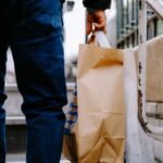 Close-up of a person carrying brown paper shopping bags on city stairs.