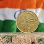 Close-up of a 5 Rupee coin commemorating India's 75th year of independence, set against the Indian flag.