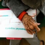 Close-up of an elderly woman holding a pen with a financial report.