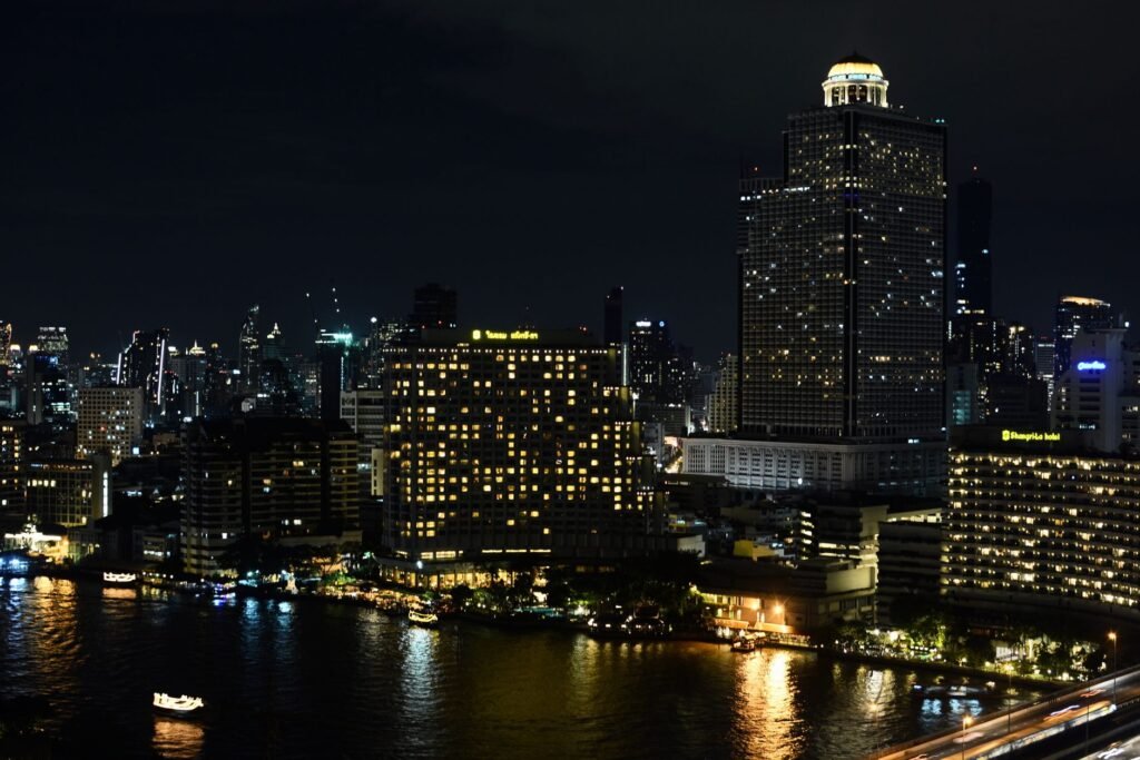 Explore the vibrant night skyline of Bangkok showcasing illuminated buildings along the riverfront, capturing the city's bustling spirit.