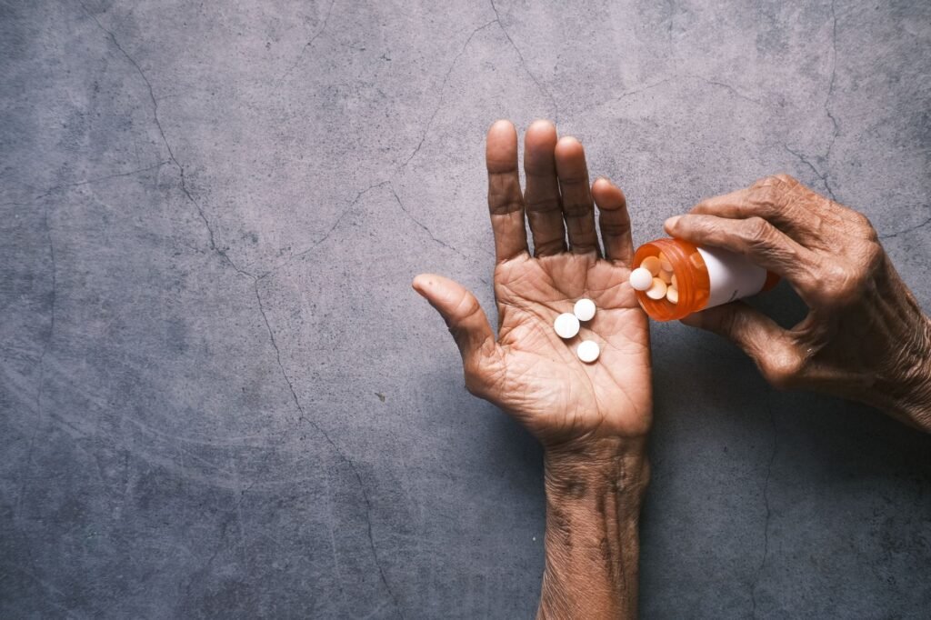 Elderly person's hand pouring pills from a bottle, offering ample copy space.