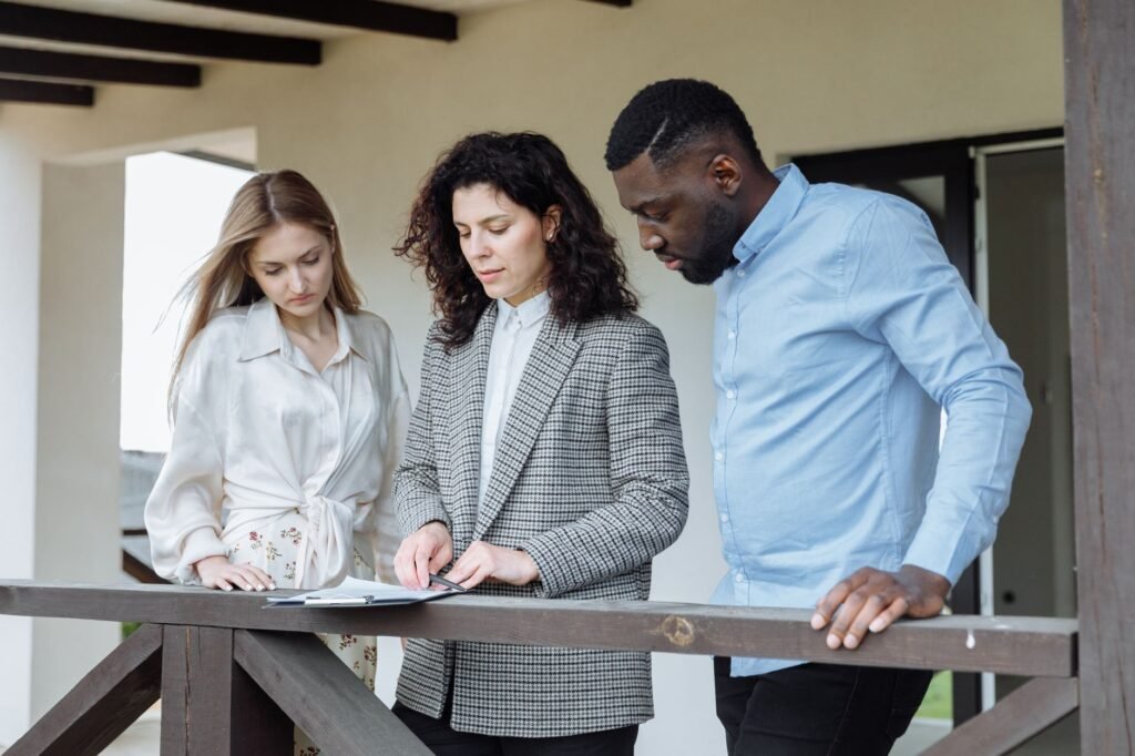 Three adults reviewing documents on a balcony during a real estate consultation.