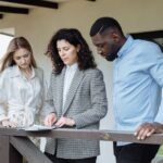 Three adults reviewing documents on a balcony during a real estate consultation.