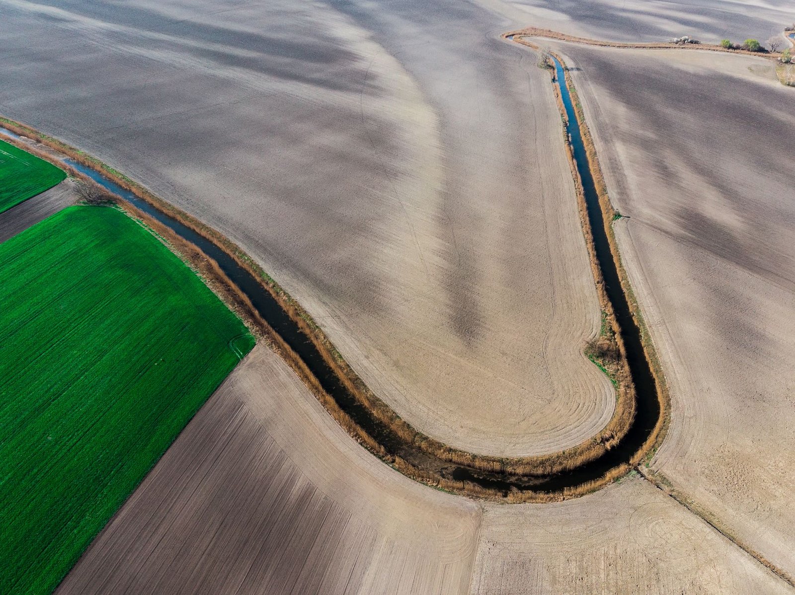High-angle drone shot showcasing vast agricultural fields and winding waterway.