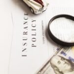 Close-up image of an insurance policy with a magnifying glass, money, and toy car.