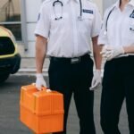 Two paramedics in uniform holding a medical kit next to an ambulance.