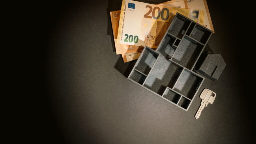 A top view of euro banknotes, a miniature architectural model, and a key symbolizing property investment.