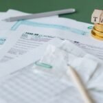 Stack of tax forms and coins with a 'TAX' stamp, symbolizing finance and accounting.