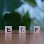 Scrabble tiles spelling ETF on a wooden surface with blurred green background.