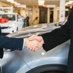 Two businessmen shaking hands in a car dealership, sealing a deal.